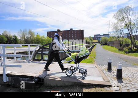 Mann, der mit Kind im Kinderwagen am Forth und Clyde Kanal, Glasgow, Schottland, läuft Stockfoto