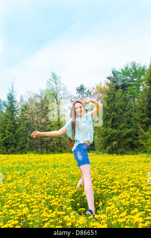 Schöne freudige glücklich attraktive unbeschwerte junge Mädchen (Frau) tanzen und springen im Sommerpark (Frühling) am gelben Löwenzahn. Stockfoto