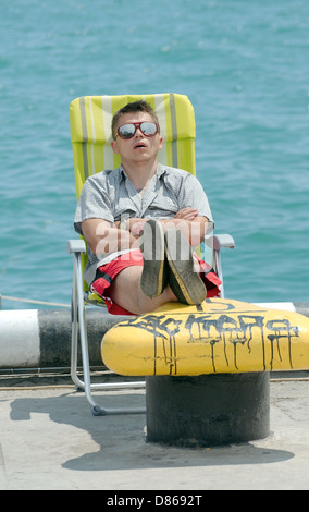 Ein junger Mann schlafen im liegen mit den Füßen oben auf einem Poller, direkt am Meer Jalta, Krim, Ukraine, Osteuropa Stockfoto