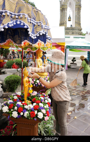 Thai Lady gießt Wasser über eine goldene sitzende Buddha-Statue während Songkran an der Wat Po Tempel des liegenden Buddha in Bangkok. Stockfoto