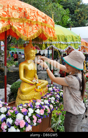 Thai Lady gießt Wasser über eine goldene sitzende Buddha-Statue während Songkran an der Wat Po Tempel des liegenden Buddha in Bangkok. Stockfoto