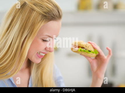 Glückliche junge Frau Essen Sandwich in Küche Stockfoto