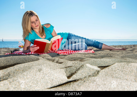 Attraktive blonde Frau ein Buch auf einem sandigen Strand an einem wunderschönen, sonnigen, Frühling Tag. Stockfoto