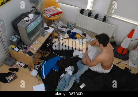 Teenager in seinem chaotischen Zimmer vor dem Fernseher Stockfoto