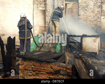 Schwelende Reste eines Ghetto-Hauses mit sprühen Wasser Feuerwehr Feuerwehrmann löschen ein Feuer in einem Mehrfamilienhaus Stockfoto