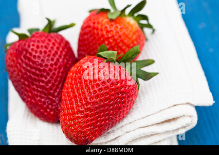 Nahaufnahme von drei großen frischen Erdbeeren ruht auf dem weißen Tuch gegen hölzerne hellblauen Hintergrund Stockfoto