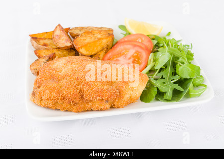 Wiener Schnitzel - Kalbssteak paniert und gebraten in Butter, serviert mit Salat, Kartoffelecken und einer Zitronenscheibe. Stockfoto