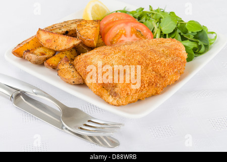 Wiener Schnitzel - Kalbssteak paniert und gebraten in Butter, serviert mit Salat, Kartoffelecken und einer Zitronenscheibe. Stockfoto