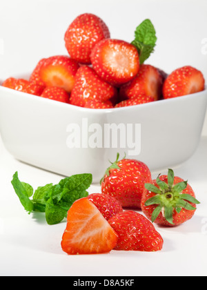 frisch geschnittene Erdbeeren und Minze Blätter auf eine weiße Schneidebrett mit einer Schüssel vorbereiteten Erdbeeren im Hintergrund Stockfoto