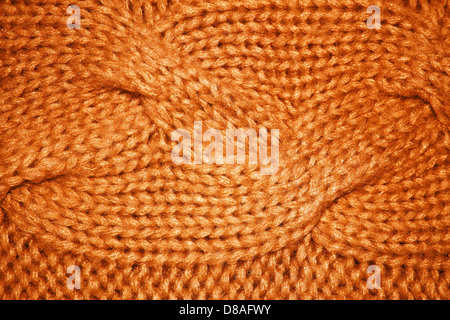 In dieser Nahaufnahme ist eine orangefarbene Struktur mit Zopfmuster zu sehen. Die komplizierte Webstruktur und die weiche Textur des Stoffes machen ihn zu einer beliebten Wahl für Strickwaren wie Pullover, Schals und Decken. Stockfoto