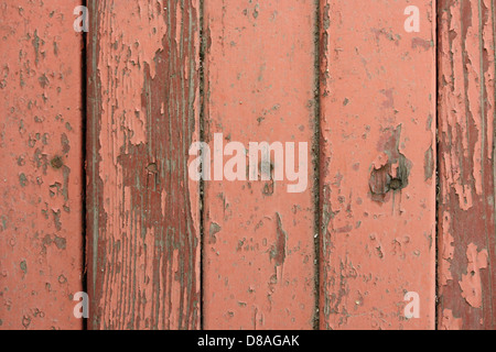 Die Textur von abblätternder roter Farbe auf alten Holzbrettern, die Schichten abgenutzter Farbe und freiliegendem Holz zeigen. Diese verwitterte Oberfläche spiegelt den Lauf der Zeit und den natürlichen Verschleiß durch die Elemente wider. Stockfoto