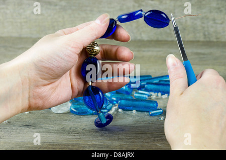 Frauenhand machen eine Halskette aus Glasperlen Stockfoto