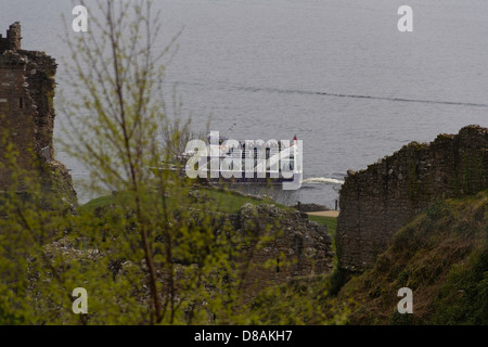 Touristen in ein Touristenboot auf dem Loch Ness durch die Ruinen von Urquhart Castle. Blick durch die zerstörten Mauern mit Anlage. Stockfoto