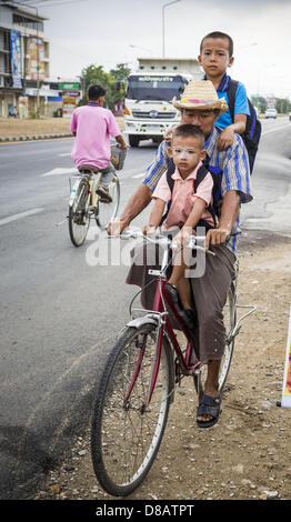 23. Mai 2013 - Mae Sot, Tak, Thailand - ein birmanischen Mann und seine Söhne auf seinem Fahrrad auf dem Asien-Highway in Mae Sot. Fünfzig Jahre der politischen Unruhen in Burma (Myanmar) hat Millionen von Burmesen ihr Land verlassen geführt. Viele haben im benachbarten Thailand niedergelassen. Mae Sot, an der Mae Nam Moie (Moie River) ist das Zentrum der birmanischen Exil lebende Gemeinschaft im zentralen Westen Thailands. Es gibt Hunderte von Tausenden von burmesischen Flüchtlingen und Migranten im Bereich. Viele Leben ein Schattendasein ohne Papiere und ohne Rückgriff, wenn sie die thailändische Behörden überqueren. Die Burmesen haben ihre eigenen Schulen und hospita Stockfoto