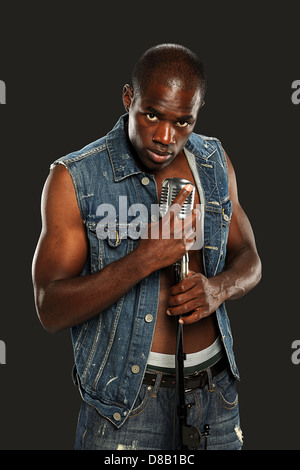 Young African American Singer hält ein Vintage Mikrofon auf einem dunklen Hintergrund isoliert Stockfoto