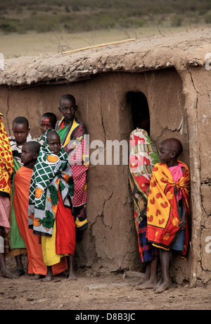 Masai Kinder tragen traditionelle Kleidung, steht man vor einer Lehmhütte in einem Dorf in der Masai Mara, Kenia, Afrika Stockfoto