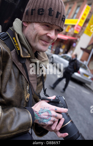 Eine Straße Fotograf mit einer Tätowierung auf seiner Hand sucht nach seinem nächsten Fototermin in Chinatown, Manchester. Stockfoto