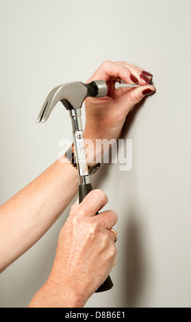 Frau mit einem Hammer auf einen Nagel in die Wand schlagen Stockfoto