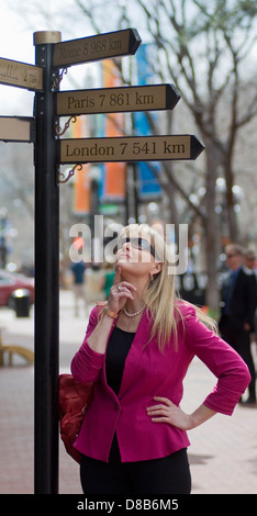 Eine Geschäftsfrau sinniert ein Zeichen nach dem Weg nach London, Rom und Paris. Stockfoto