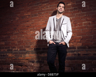 Porträt eines modischen lächelnden jungen Mannes tragen leichte graue Blazer und schwarze Jeans stehen an einer Mauer Stockfoto