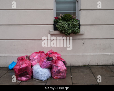 Säcke mit Müll sitzen auf einer städtischen Straße in der Nähe eine Wohnimmobilie. Stockfoto