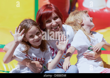 Junge Mutter mit ihrem süßen Töchter winken Sie auf der Hüpfburg, im Freien in einem hellen, sonnigen Tag lachend. glückliche Familie sieht genauso aus wie dieses! Stockfoto