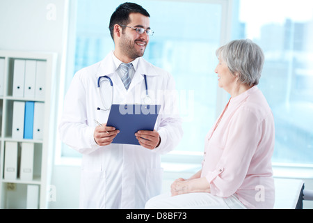 Zuversichtlich Arzt mit Stethoskop und Zwischenablage Interaktion mit seinem älteren Patienten im Krankenhaus Stockfoto