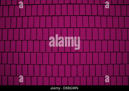 Ein Nahbild einer magentafarbenen Ziegelwand mit vertikal ausgerichteten Ziegeln. Die Textur der Steine und die leuchtende Farbe sind in dieser detailreichen Aufnahme deutlich sichtbar. Stockfoto