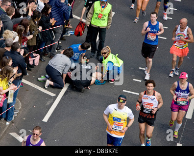 Veranstalter und St John Ambulance helfen einen eingestürzten männlichen Konkurrenten im Jahr 2013 London Marathon Victoria Embankment England Europa Stockfoto