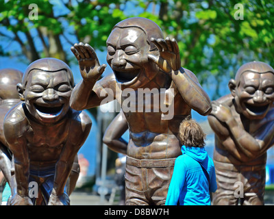 Ein Passant untersucht die lachende Männer Statuen in Vancouver, Kanada Stockfoto