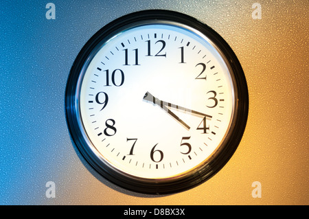Schwarz-weiß-Uhr auf Wand mit Licht und Schatten als Symbol für Tag und Nacht. Üblichen Uhr auf zwei-farbigen Hintergrund: blau Stockfoto