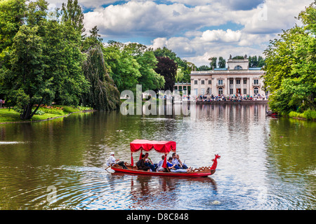 Touristen genießen eine Gondelfahrt auf dem See im Łazienki Park Łazienkowski, größte in Warschau mit dem Palast im Hintergrund. Stockfoto
