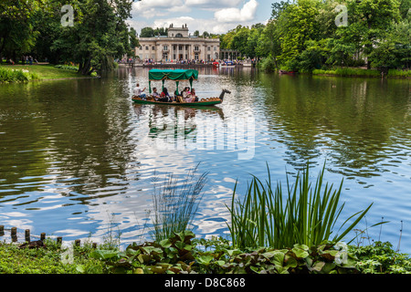 Touristen genießen eine Gondelfahrt auf dem See im Łazienki Park Łazienkowski, größte in Warschau mit dem Palast im Hintergrund. Stockfoto
