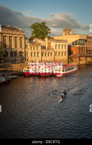 Eine Flotte von Kreuzfahrt- und Touristenbooten, die an einem sonnigen Sommerabend an der Guildhall mit einem Ruderboot im Vordergrund vor Anker liegt. River Ouse, York. Stockfoto