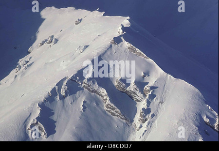 Ein Blick aus der Vogelperspektive auf einen Berggipfel mit umliegenden malerischen Landschaften. Das Bild fängt die atemberaubende Schönheit des Geländes ein und zeigt schroffe Klippen, Schnee und Täler darunter. Stockfoto