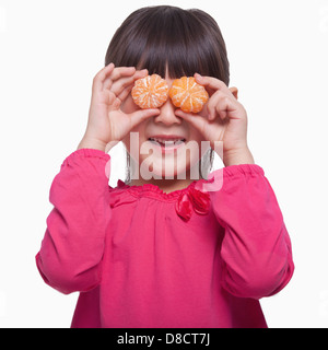 Kleines Mädchen hält Mandarinen vor ihren Augen Studio gedreht Stockfoto