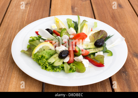 Griechischer Salat mit Feta, Tomaten, Gurken, Paprika und schwarzen Oliven auf einem Holztisch. Stockfoto