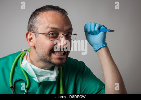 Lustige verrückte Arzt in grüner Uniform mit einem chirurgischen Messer Stockfoto