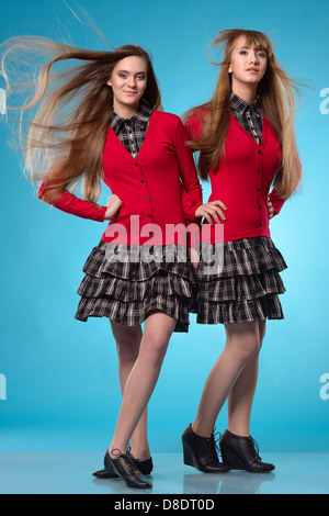 Zwei Teenie Schulmädchen stehen Seite an Seite über Studio blauen Hintergrund. Wind weht auf Haare Stockfoto