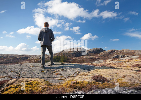 Junger Mann auf dem Felsen steht und schaut über den Horizont Stockfoto