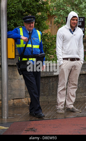 Zivilschutzbeamter und Mann im Hoodie warten im Mai bei Regen an der Ampel in Oxford, Oxfordshire, Großbritannien Stockfoto