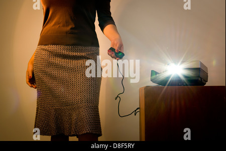 Retro-Stil Frau einen Dia-Projektor mit einer Kabelfernbedienung und Reflexlicht von Projektorlicht in Betrieb Stockfoto