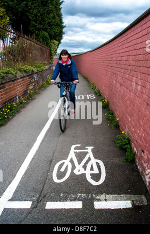 Reife kaukasische Frau, die auf einem schmalen Radweg Fahrrad fährt. Stockfoto