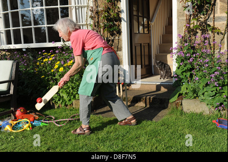 Ältere Großmutter ein Spiel Cricket im Garten für ihre Familie zu Hause in North Yorkshire. Stockfoto