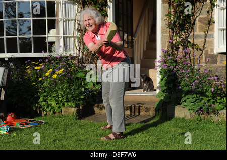 Ältere Großmutter ein Spiel Cricket im Garten für ihre Familie zu Hause in North Yorkshire. Stockfoto