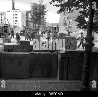 Bauarbeiter der Ost-Berliner reichen von "Potsdamer Platz" Platz in Richtung der "Lindenstraße" Straße unter der Aufsicht von bewaffneten Offizieren der Volkspolizei in Berlin, DDR, 18. August 1961 die Berliner Mauer. Die Mauer ist zwischen zwei und fünf Metern innerhalb der Demarkationslinie der Sektoren in Ost-Berlin. Hier verlaufen die Grenzen der Sektoren auf die Hausfassaden. Grit Betonplatten und hohle Ziegelsteine, die zunächst für den Bau von Häusern in Ost-Berlin konzipiert wurden, werden für den Bau verwendet. Die Bauarbeiter sind 1,28 DM pro Stunde bezahlt. In Stockfoto