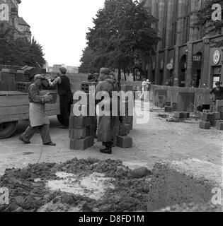 Bauarbeiter der Ost-Berliner reichen von "Potsdamer Platz" Platz in Richtung der "Lindenstraße" Straße unter der Aufsicht von bewaffneten Offizieren der Volkspolizei in Berlin, DDR, 18. August 1961 die Berliner Mauer. Die Mauer ist zwischen zwei und fünf Metern innerhalb der Demarkationslinie der Sektoren in Ost-Berlin. Hier verlaufen die Grenzen der Sektoren auf die Hausfassaden. Grit Betonplatten und hohle Ziegelsteine, die zunächst für den Bau von Häusern in Ost-Berlin konzipiert wurden, werden für den Bau verwendet. Die Bauarbeiter sind 1,28 DM pro Stunde bezahlt. In Stockfoto