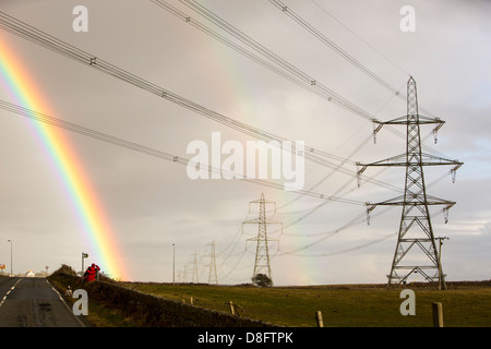 Ein Regenbogen über Strommasten Kernkraftwerk Wylfa auf Anglesey, Wales, UK verlassen. Stockfoto