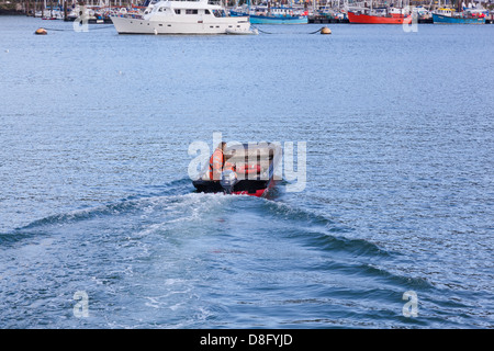 Mann gekleidet in hi-viz orange Jacke Segeln über den Fluss Dart in Dartmouth in einem kleinen Schlauchboot mit Außenbordmotor. Stockfoto