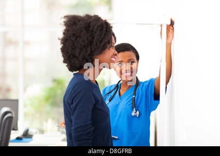 freundlichen afrikanischen Krankenschwester, die Messung der Höhe des Patienten Stockfoto